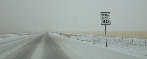 Snow covered road with a Speed Limit 80 sign nexxt to it.