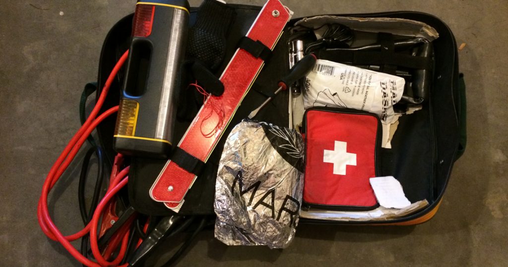 Contents of an emergency kit are spread out including a medical kit, flash light and emergency blanket