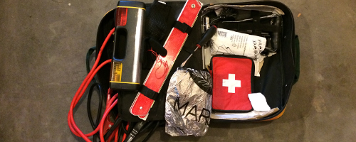 Contents of an emergency kit are spread out including a medical kit, flash light and emergency blanket