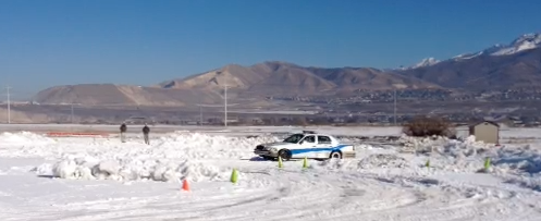 An old Crown Victoria is on a snow covered driving cause with mountains in the background.