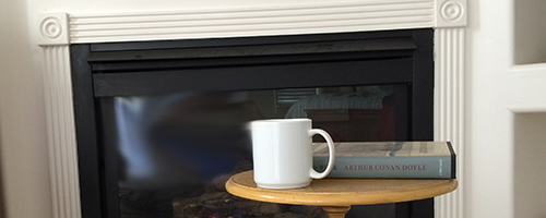 Coffee cup and a book sit on a table in front of a fire place.