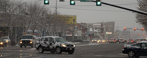 Cars with snow on them turn left in downtown Salt Lake City.
