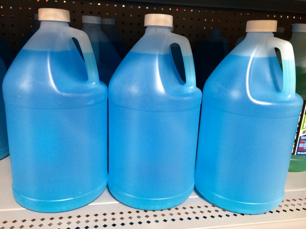 Three bottles of bright blue wiper fluid sit on a shelf