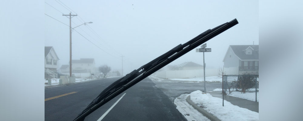 A windshield wiper moves across a windshield from the driver's view onto a snowy road.